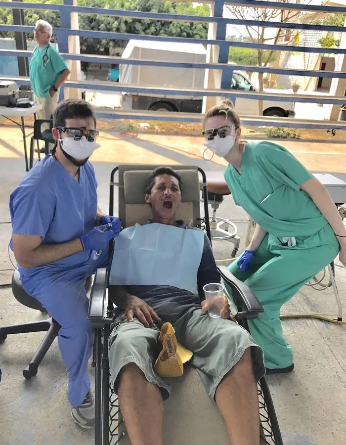 Two masked members of the mission team treating a patient in a reclining chair, 2016.